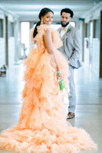 A stunning bride wearing orange dress by Milla London while the groom admiringly looking at his bride inside the hallway of Abbey Road Farms in Carlton, Oregon