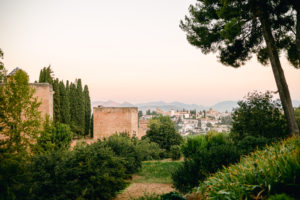 Sunset tan building overlooking city view of Granada. Garden entrance of Alhambra Palace in Granada, Spain Cypress trees 