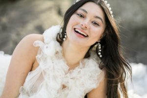 A laughing bride with pearl earrings and head piece with hair down, she is wearing a bridal tulle puffy Milla London wedding dress